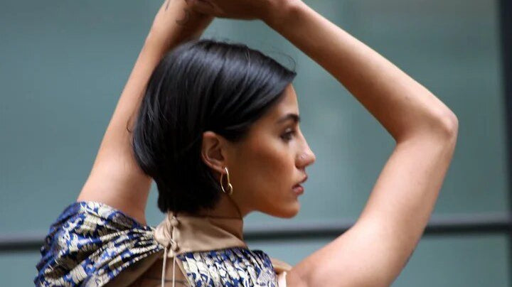 a model with arms raised in a gold dress with blue shoulder details