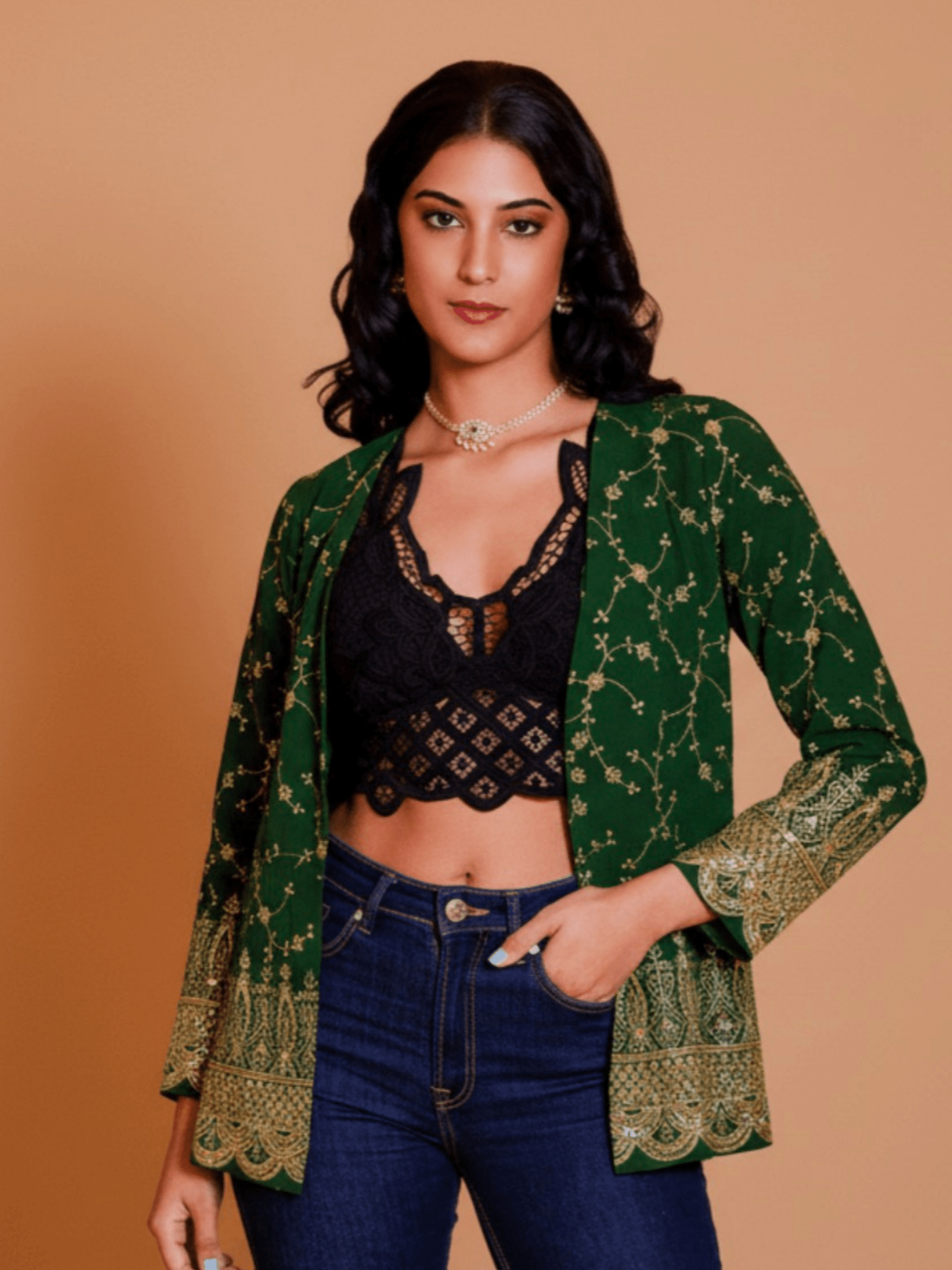 Woman wearing a green patterned jacket over a black top and blue jeans on a beige background