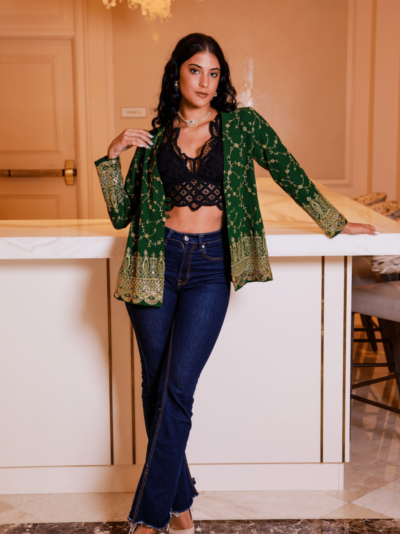 Woman wearing a green patterned jacket over a black top and blue jeans in an indoor setting.