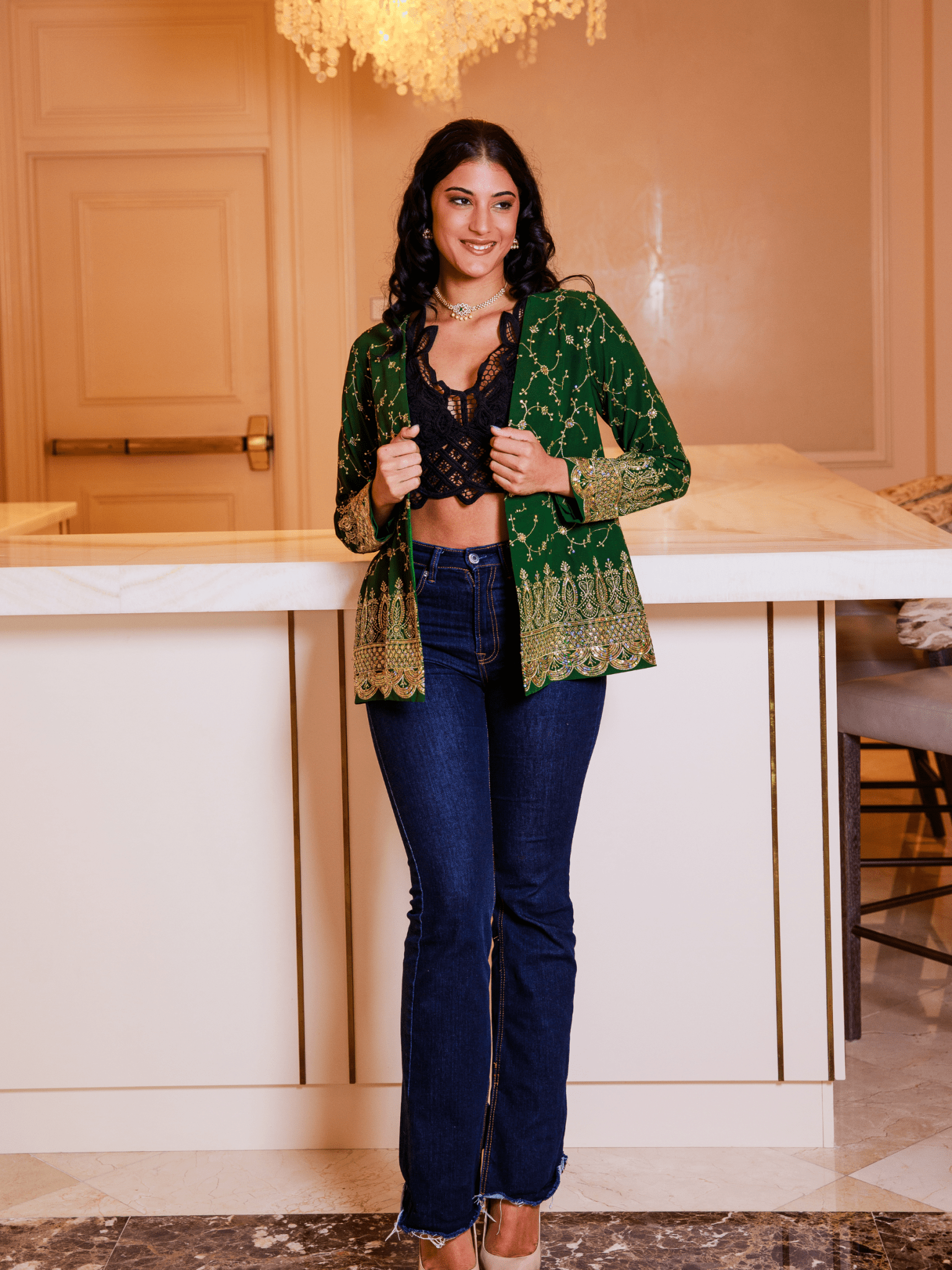 Woman wearing a green patterned jacket over a black top and blue jeans in an indoor setting.