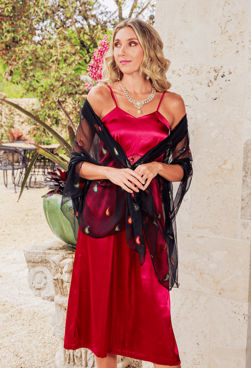 Woman in a red dress with a black shawl standing outdoors near a stone wall.