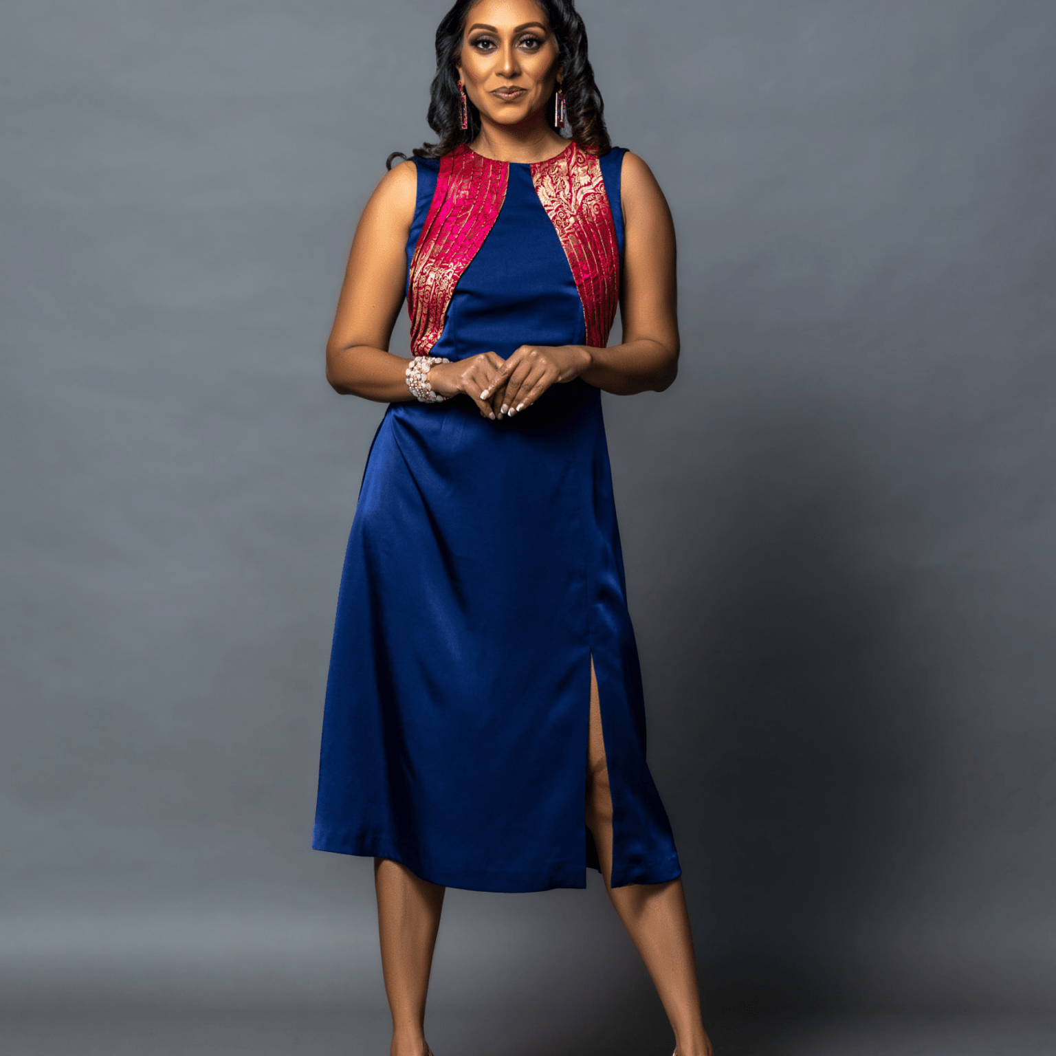 Woman wearing a blue dress with a red vest against a gray background