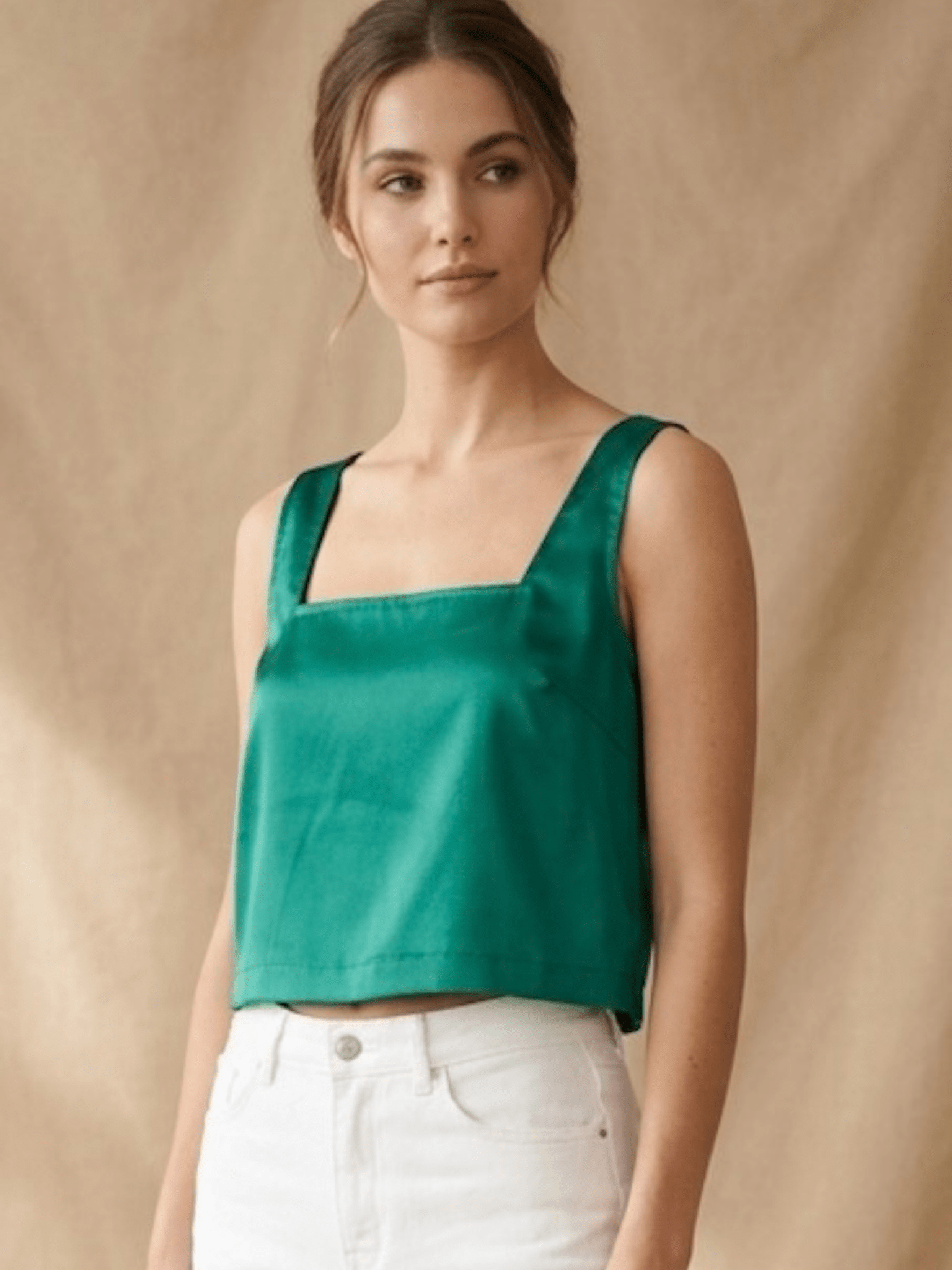 Woman wearing a green top and white pants against a beige background