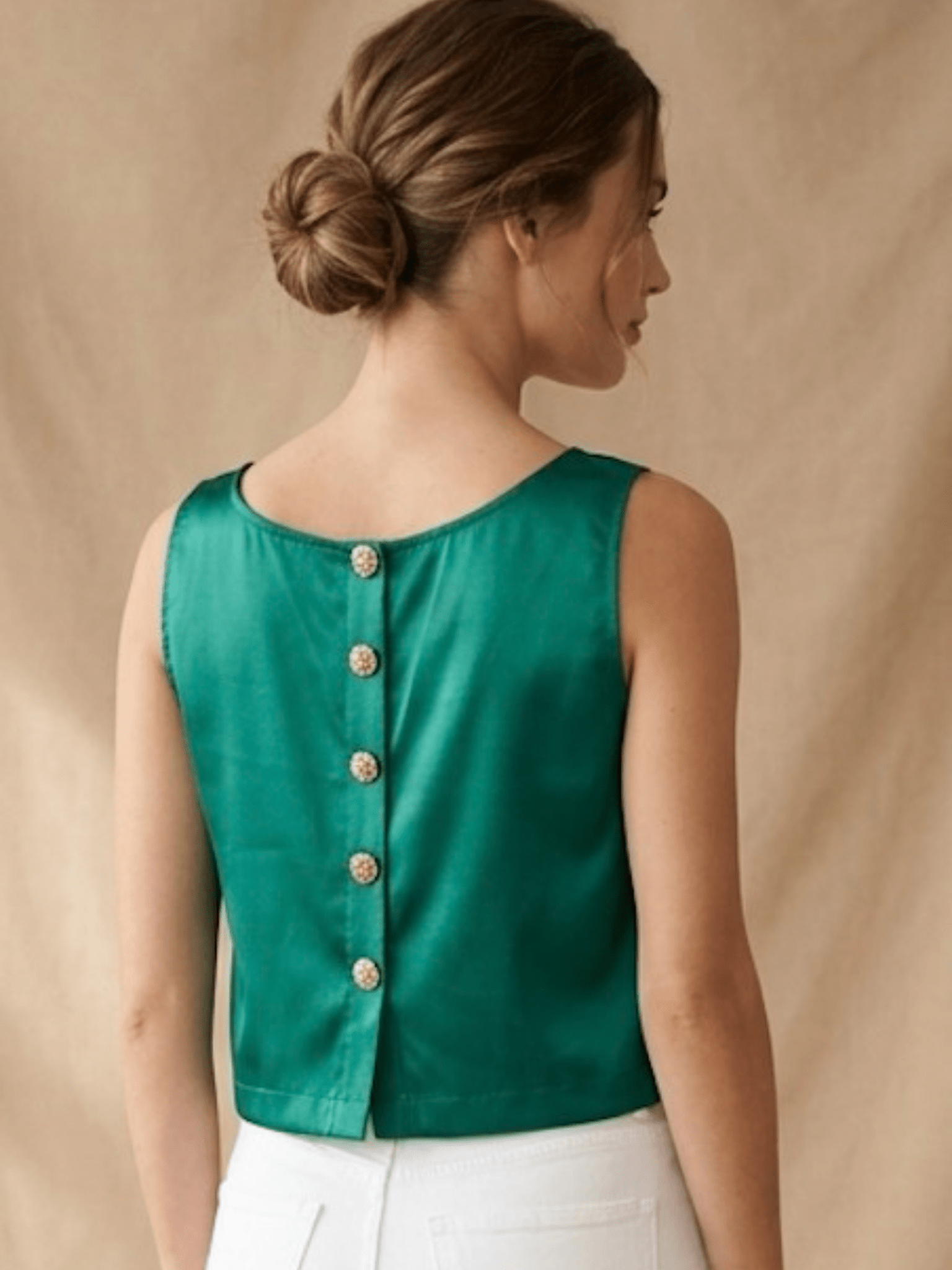 Woman wearing a green sleeveless top with button details on a beige background