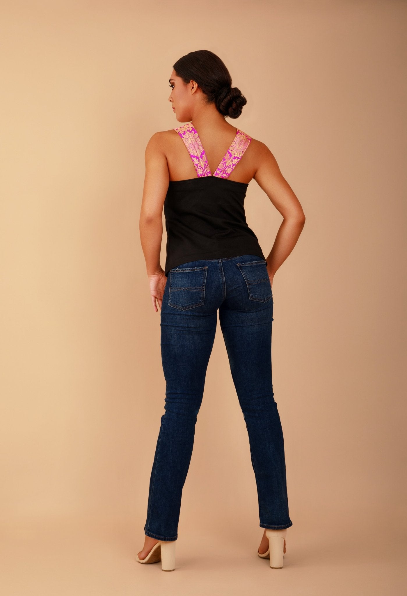 Woman wearing a black top and blue jeans against a beige background