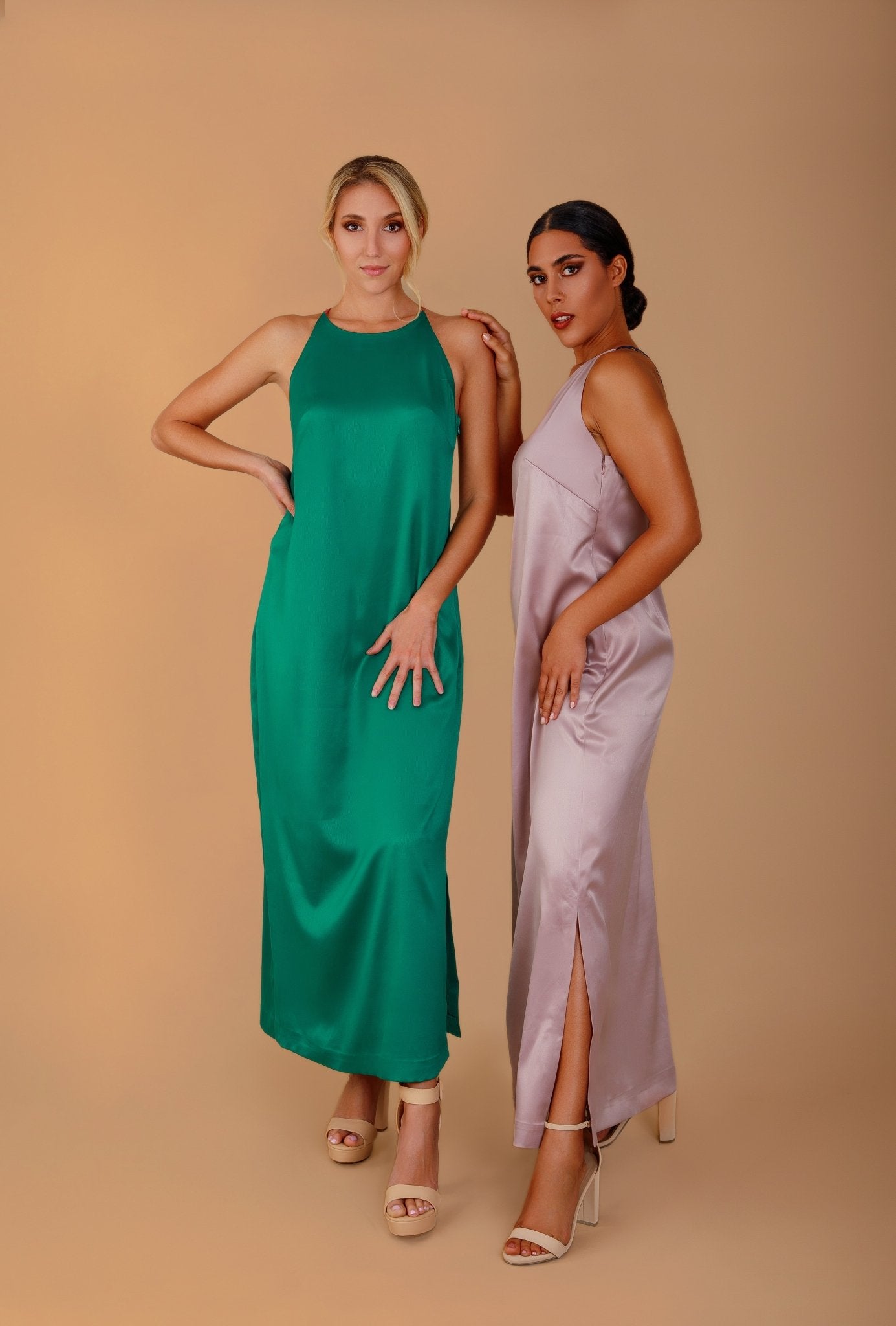 Two women wearing green and pink satin dresses against a beige background