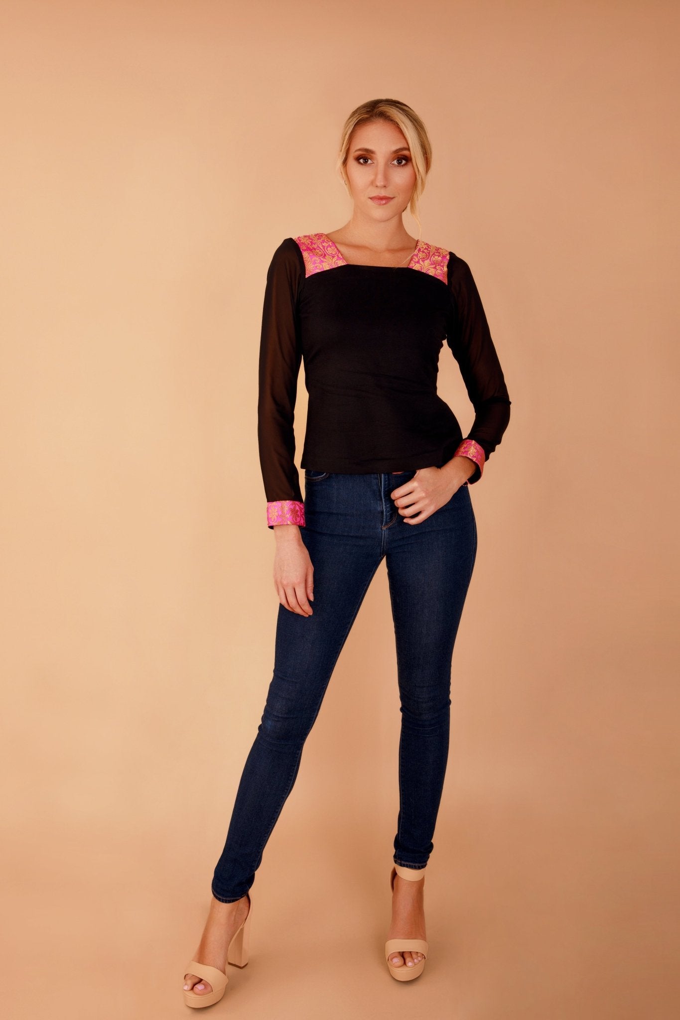 Woman wearing a black top with pink accents and blue jeans on a beige background