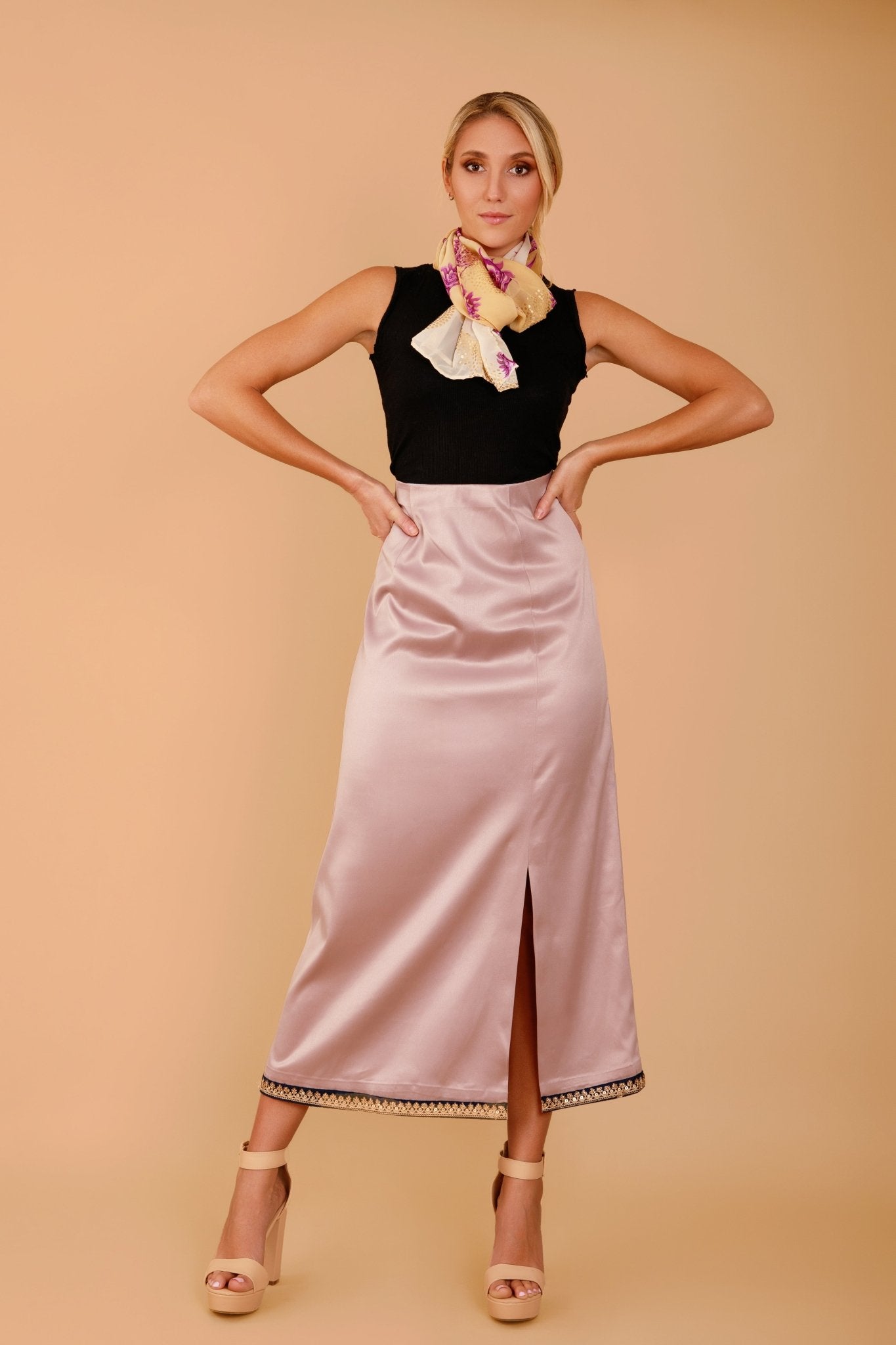 Woman wearing a black top and pink satin skirt against a beige background