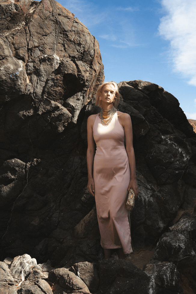 Woman in a pink dress standing among large rocks with a blue sky.