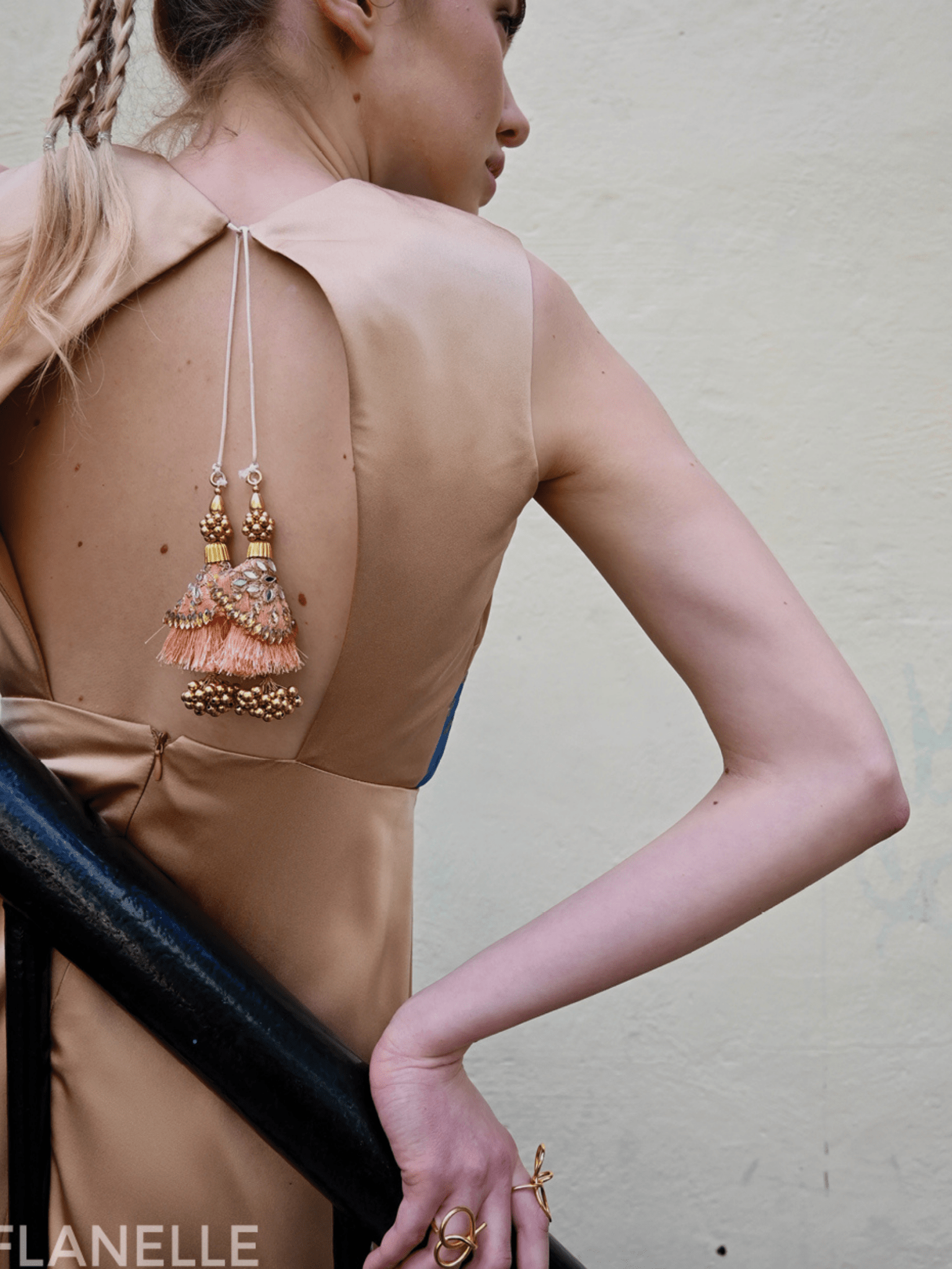 Woman wearing a beige dress with intricate gold earrings and jewelry, standing against a plain background.