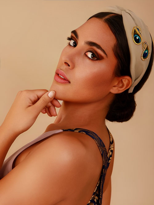a model wearing a beige headband with a beaded peacock detail