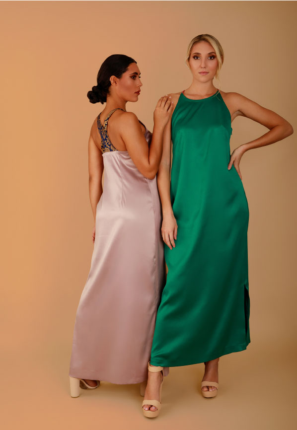 two models wearing long satin dresses in light pink and green