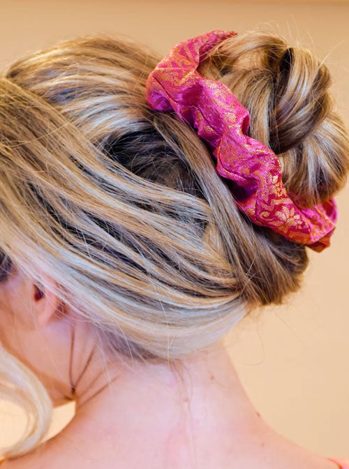 a woman with blonde hair wearing a pink scrunchie with a gold pattern
