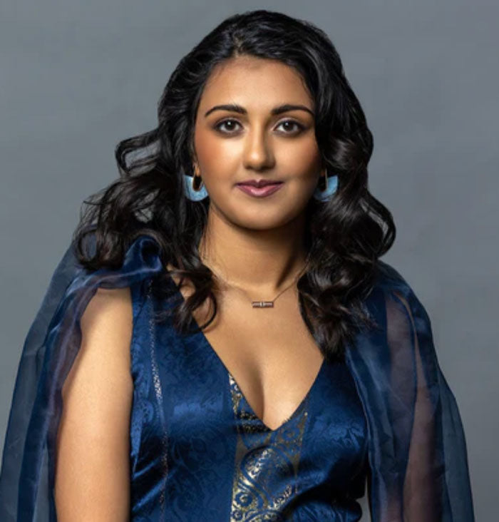 a woman with dark curled hair wearing a navy blue v-neck dress with a tulle shawl detail