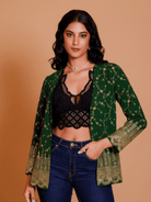 Woman wearing a green patterned jacket over a black top and blue jeans on a beige background