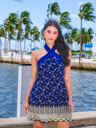 Woman in a blue dress standing by a waterfront with palm trees in the background