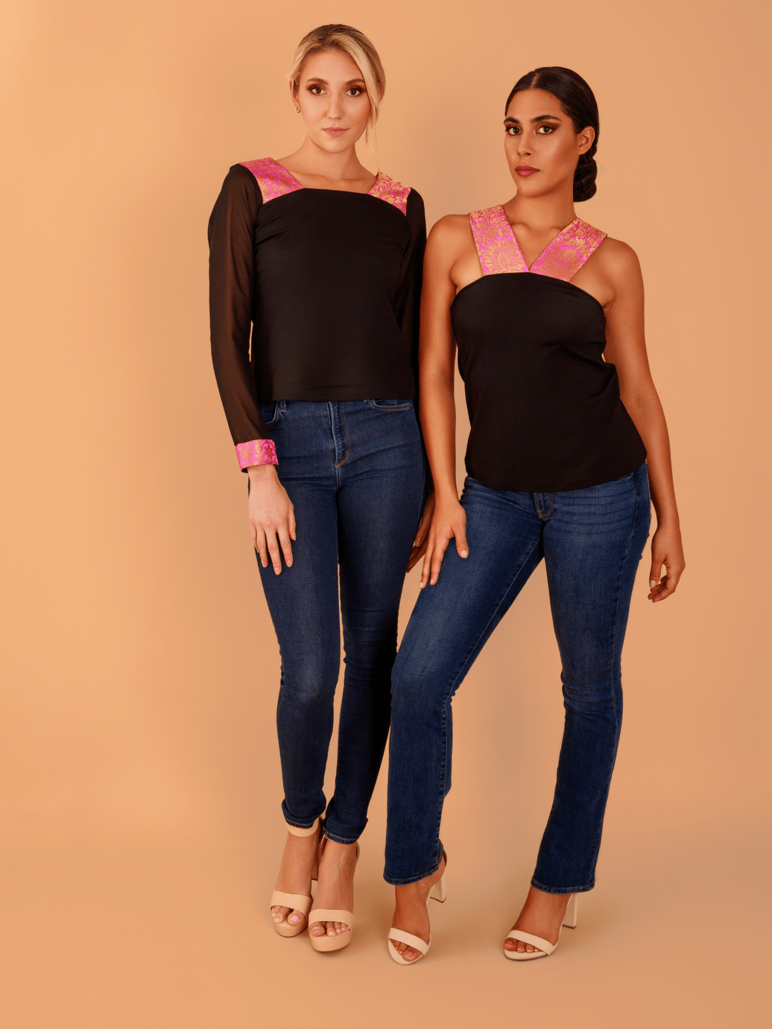 Two women wearing matching black tops with pink accents and blue jeans on a beige background