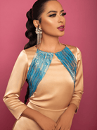 Woman wearing a beige dress with blue patterned shoulders against a pink background