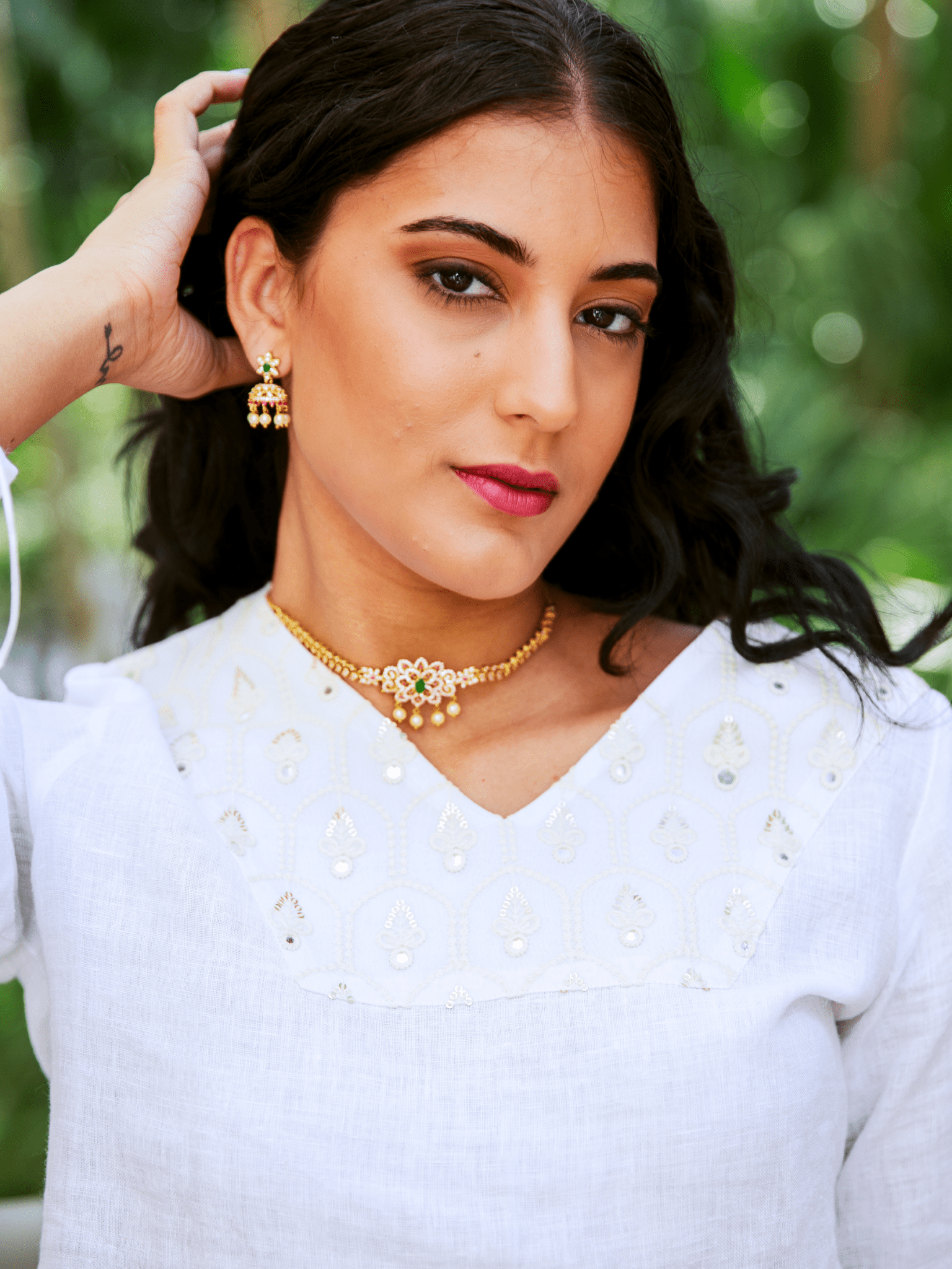 Woman wearing a white traditional outfit with gold jewelry against a blurred green background