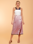 Woman wearing a white top and pink skirt with a beige background