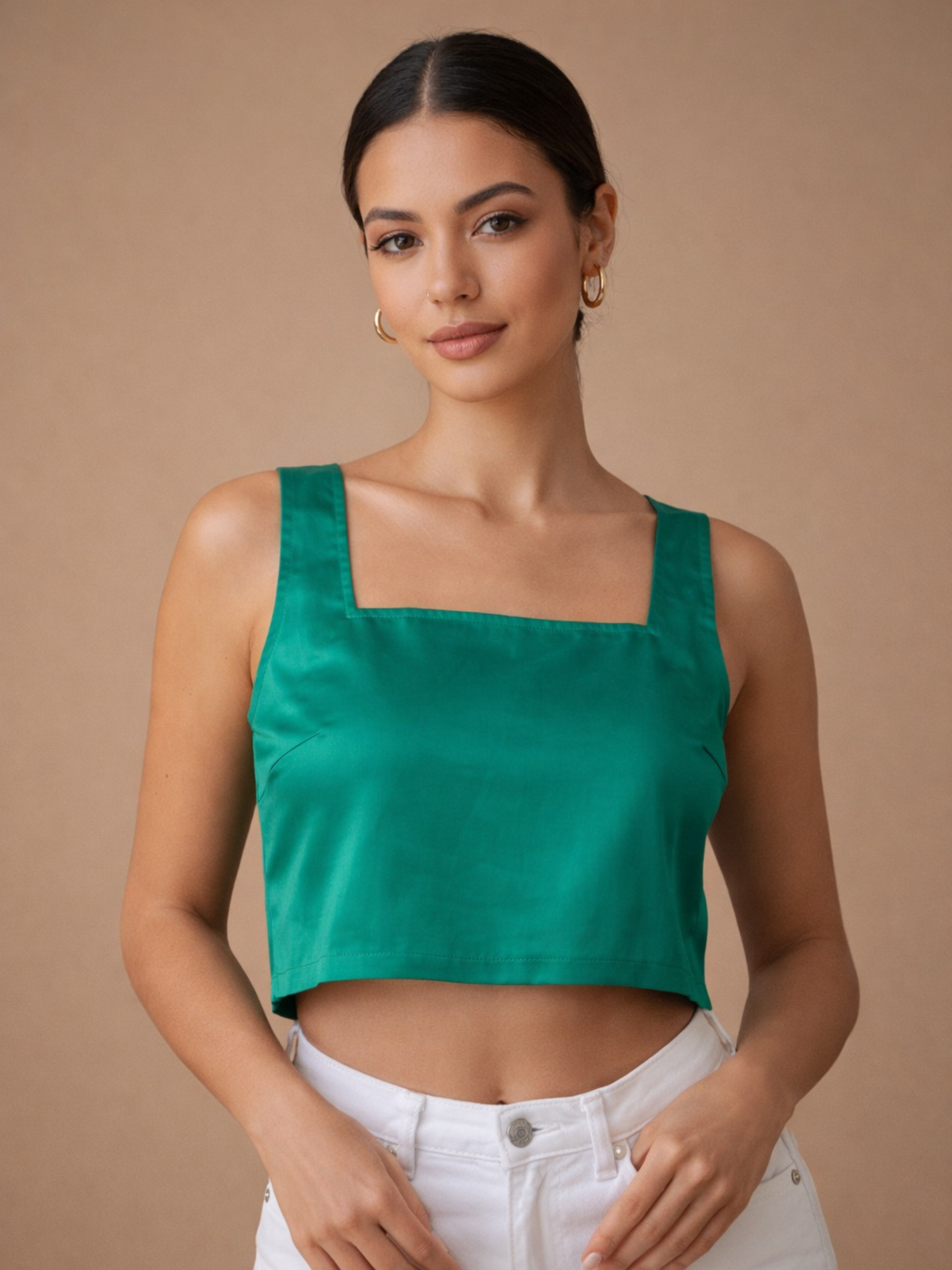 Woman wearing a green crop top and white pants against a beige background