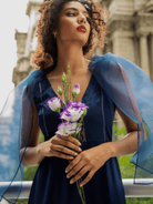 Woman holding flowers with a blue shawl in an outdoor setting