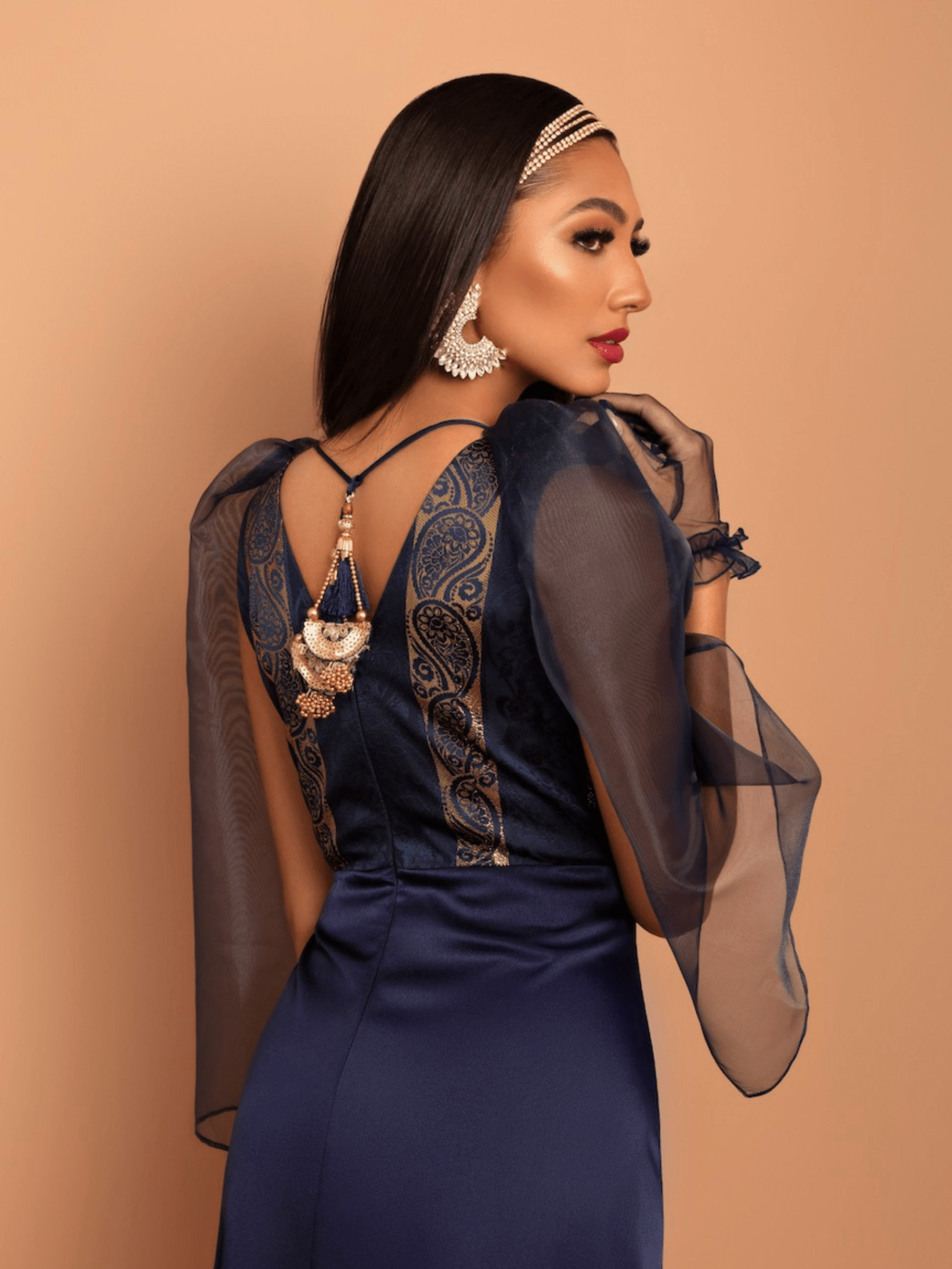 Woman wearing a dark blue dress with sheer sleeves and gold detailing on a beige background