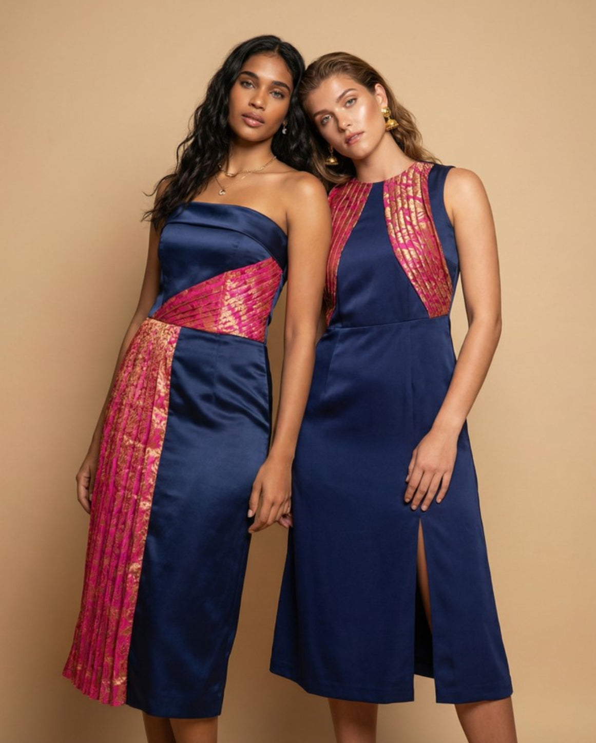 Two women wearing matching blue and pink dresses against a beige background