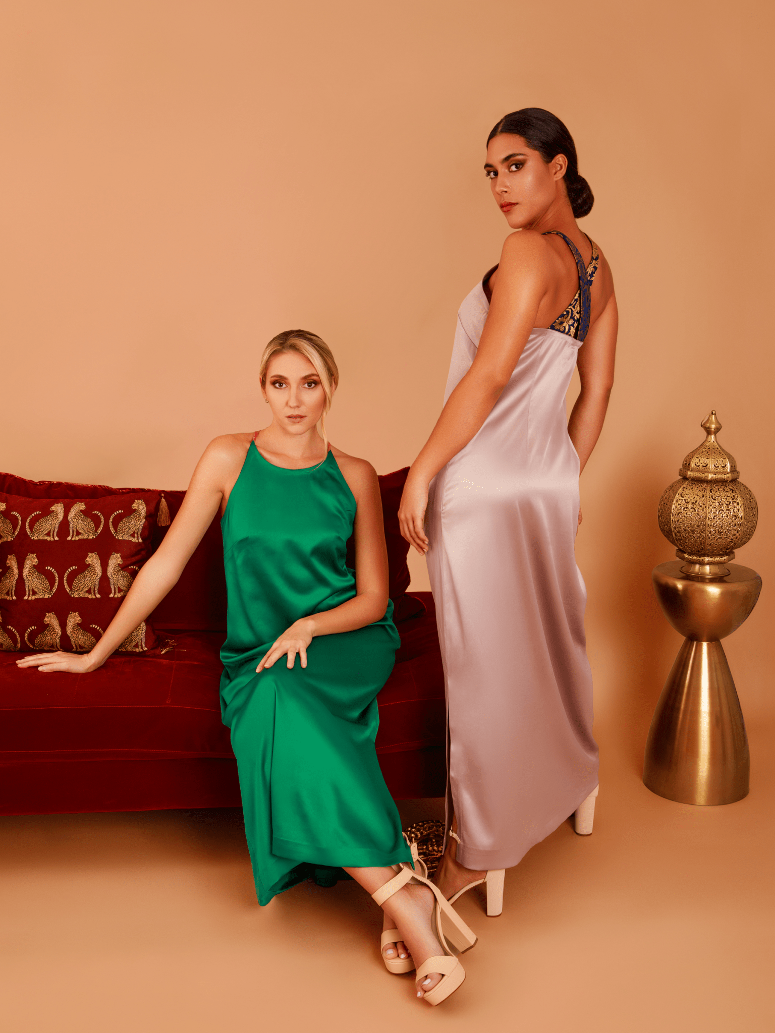 Two women in elegant dresses posing against a beige background with decorative elements.