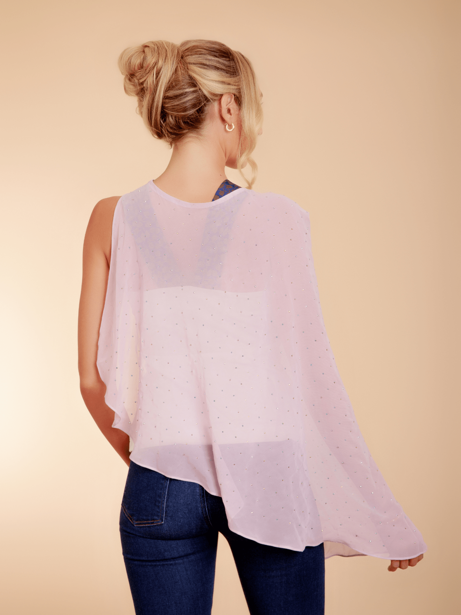 Woman wearing a light pink poncho over a white top and blue jeans on a beige background