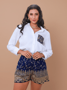 Woman wearing a white shirt and blue patterned shorts on a beige background