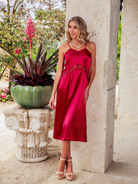Woman in a red dress standing next to a stone column with plants in the background