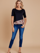 Woman wearing a black top with a floral pattern and blue jeans on a beige background