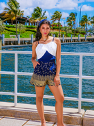 Woman in a white and blue top with patterned shorts standing by a waterfront.