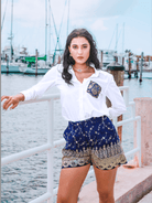 Woman in a white shirt and blue shorts standing by a waterfront with boats in the background