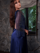 Woman wearing a blue outfit with a stone wall and greenery background