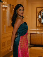 Woman in a strapless teal and pink dress standing in an elegant room with gold walls.