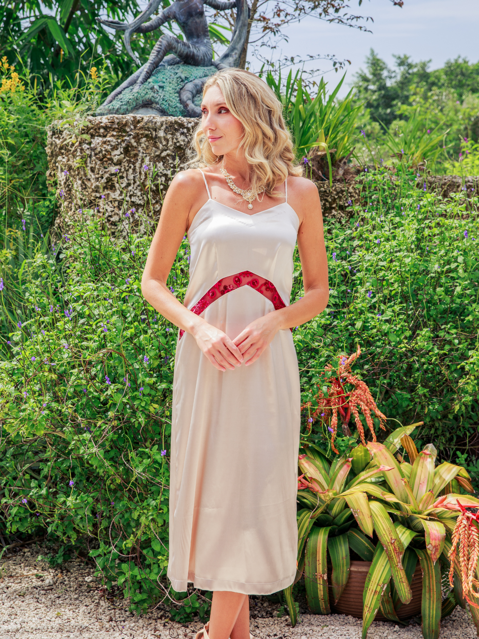Woman in a white dress with red trim standing in a garden setting