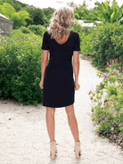 Woman in a black dress walking along a garden path with greenery and flowers.