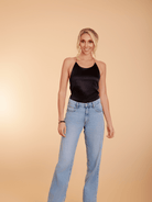 Woman wearing a black tank top and blue jeans against a beige background