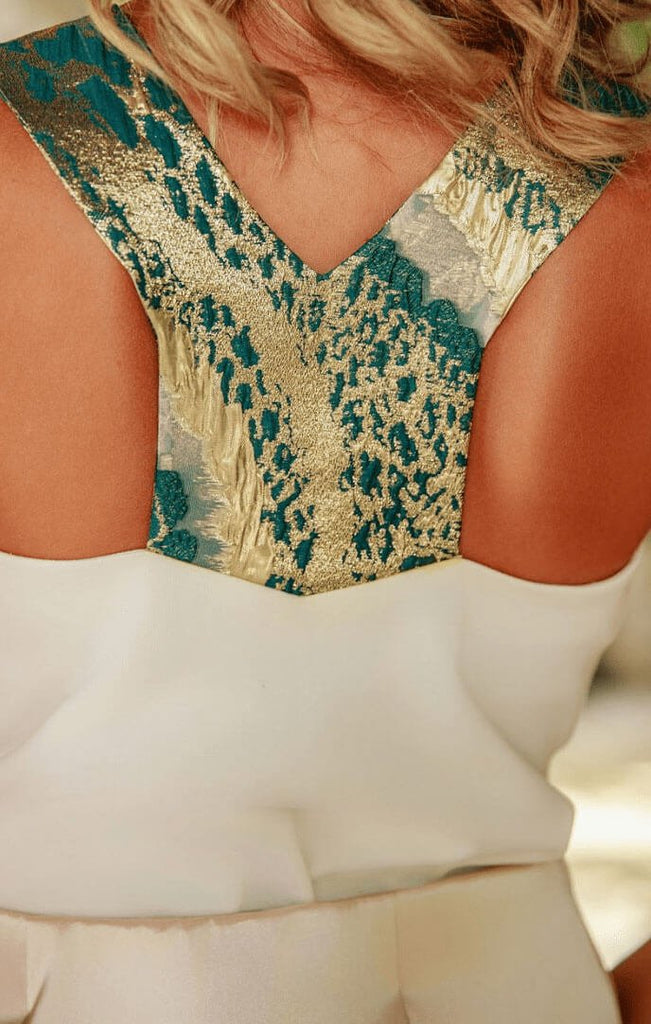 The back of a cream top with floral green and gold strap details