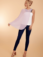 Woman wearing a sleeveless top with a sheer overlay and dark jeans on a beige background