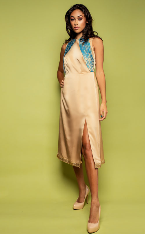 a model in a gold dress with blue details against a green backdrop