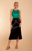 a model in a green satin halter top and a black satin midi skirt