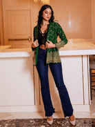 Woman wearing a green patterned top and blue jeans in an indoor setting.
