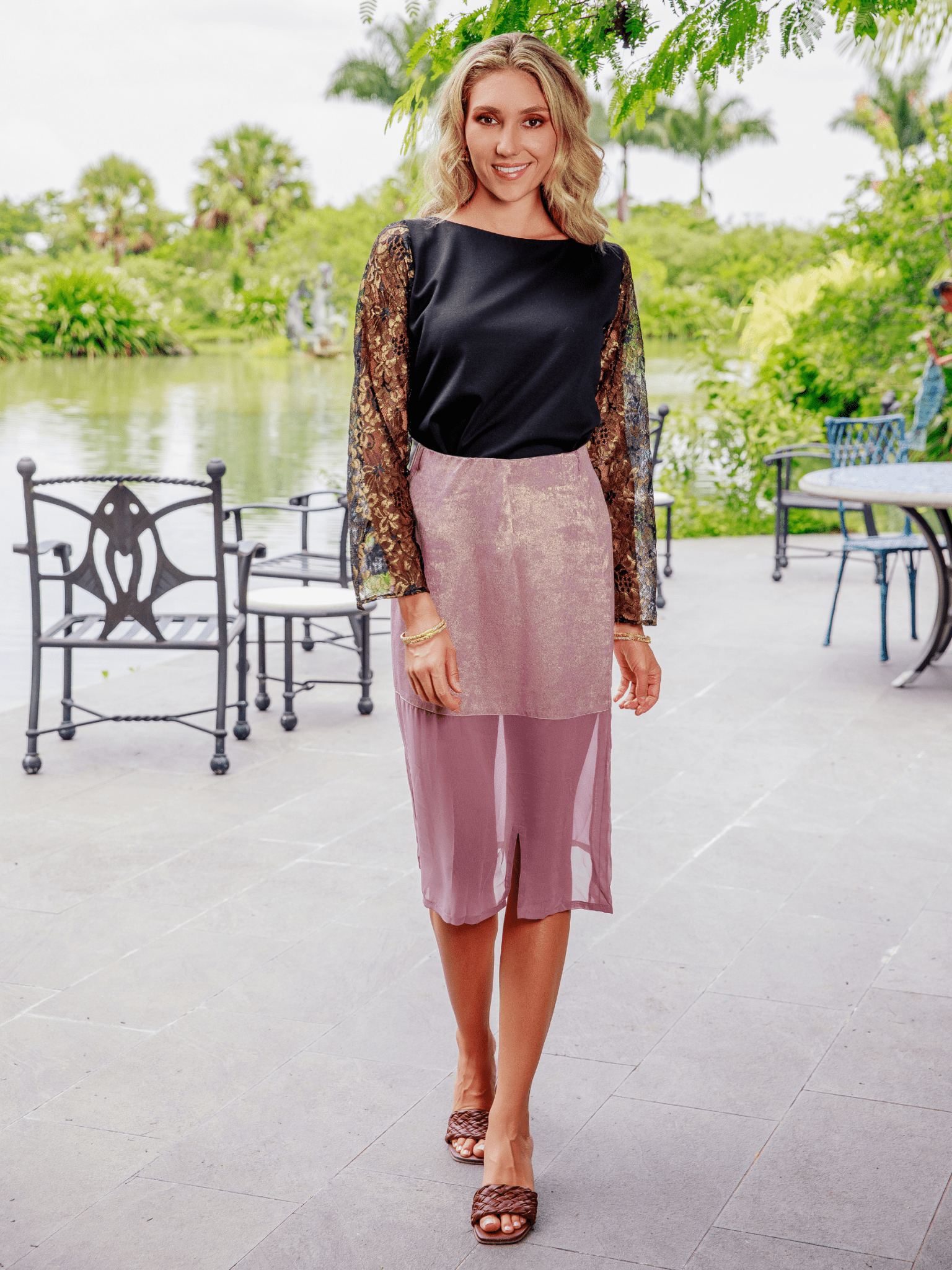 Woman in a black top and pink skirt standing outdoors with greenery in the background