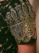 Close-up of a green garment with intricate gold embroidery and beadwork.