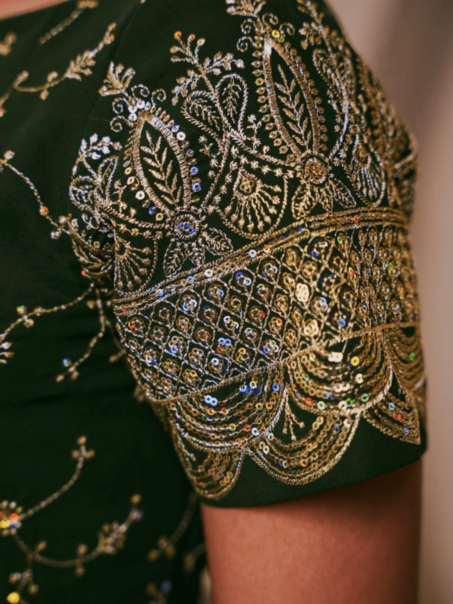 Close-up of a green garment with intricate gold embroidery and beadwork.