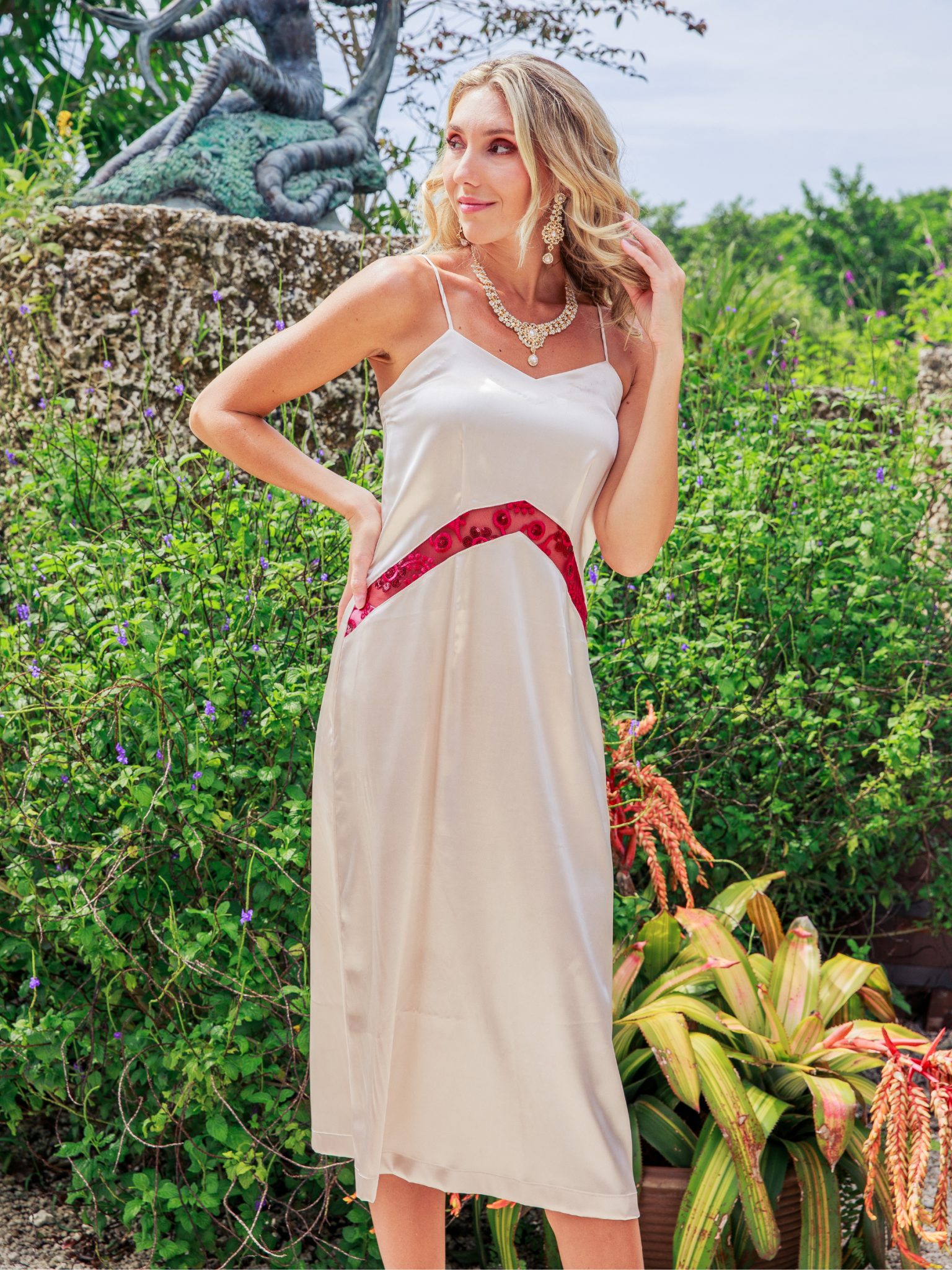 Woman in a white dress with red accents standing in a garden setting